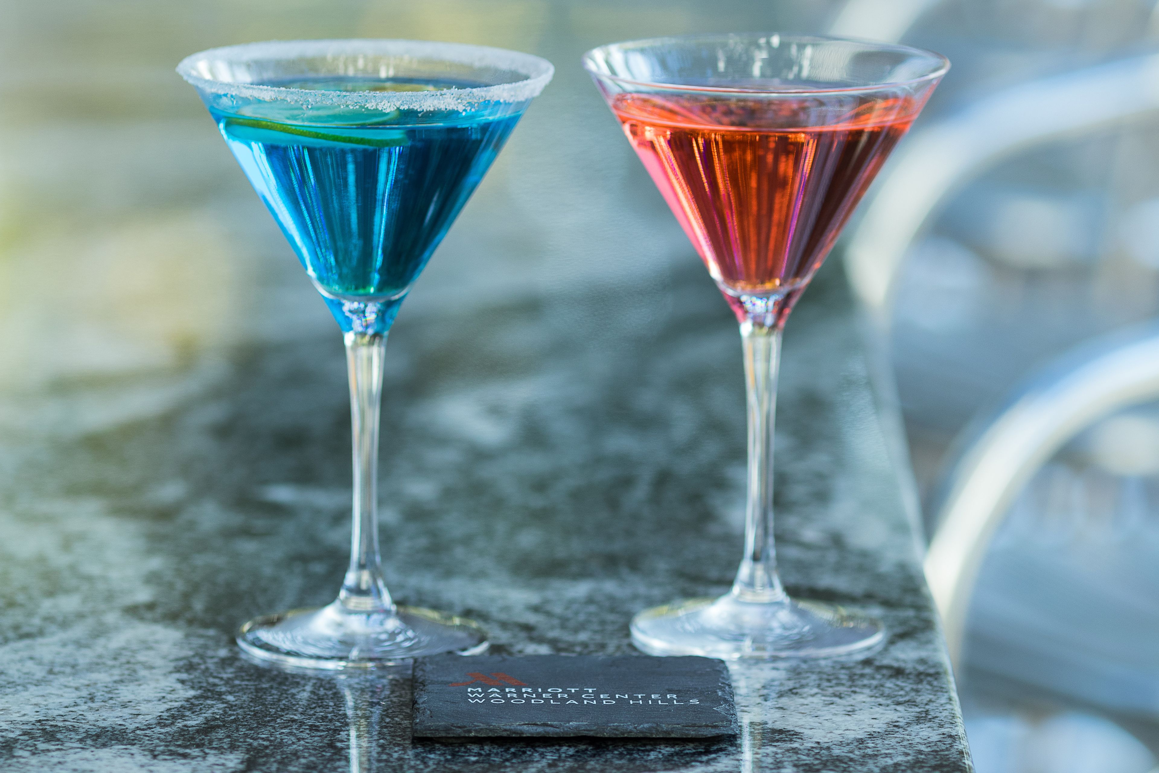Two martini glasses with blue and red liquids on a marble surface.