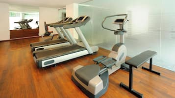 Een sportschool met loopbanden, een crosstrainer en een bankje.
