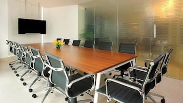 A conference room with a long table, black office chairs, a flat-screen TV, and a glass partition with frosted patterns.