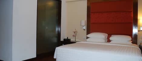 Habitación de hotel con una cama grande, una mesita de noche, una lámpara y una pared de acento roja.