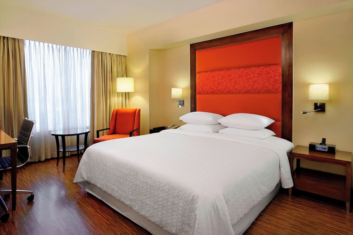 A hotel room with a large bed, a desk with a chair, a small table, and two lamps.