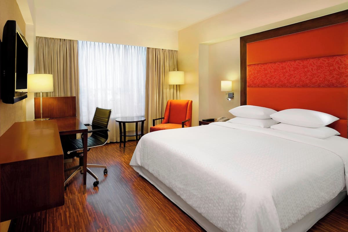 A hotel room with a large bed, a desk, a chair, and a television.