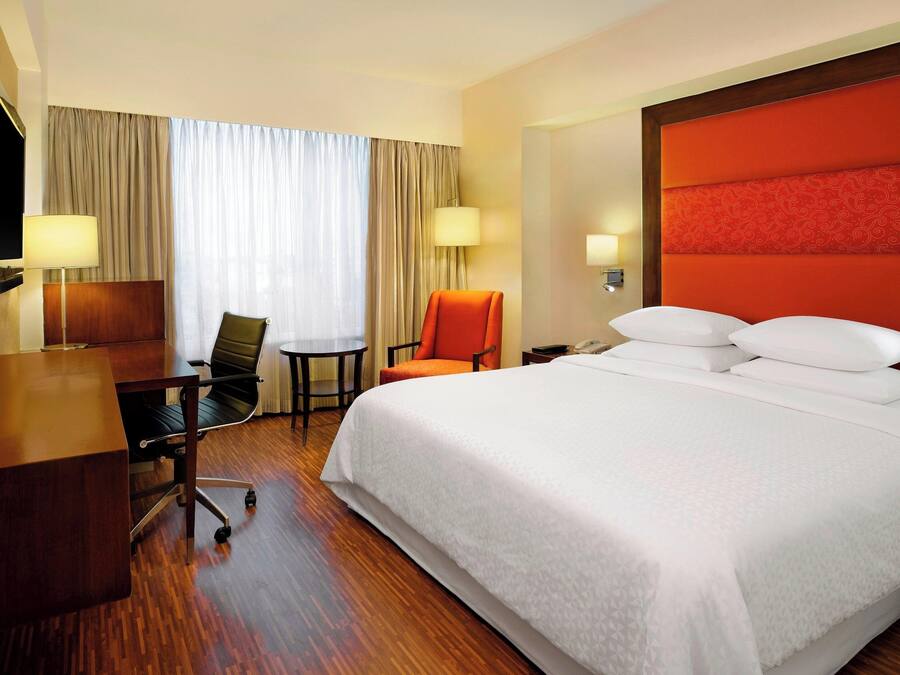 A hotel room with a large bed, a desk, a chair, and a television.