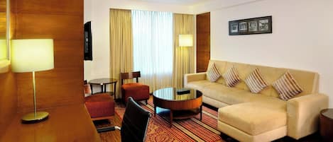 Habitación de hotel con sofá, sillón, mesa de centro y escritorio con lámpara.