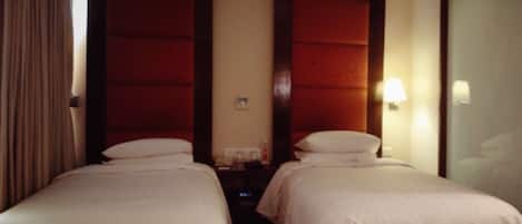 Una camera d'albergo con due letti singoli, un comodino, una lampada e un armadio.