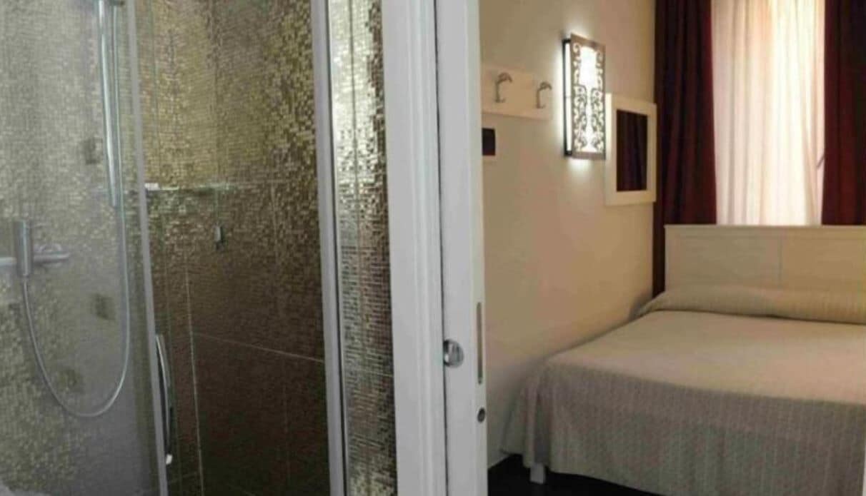 Una habitación de hotel con ducha, cama y ventana con cortinas.