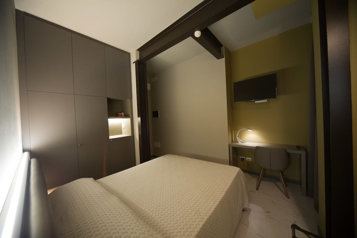 A bedroom with a bed, a desk, a chair, a TV, and a wardrobe.