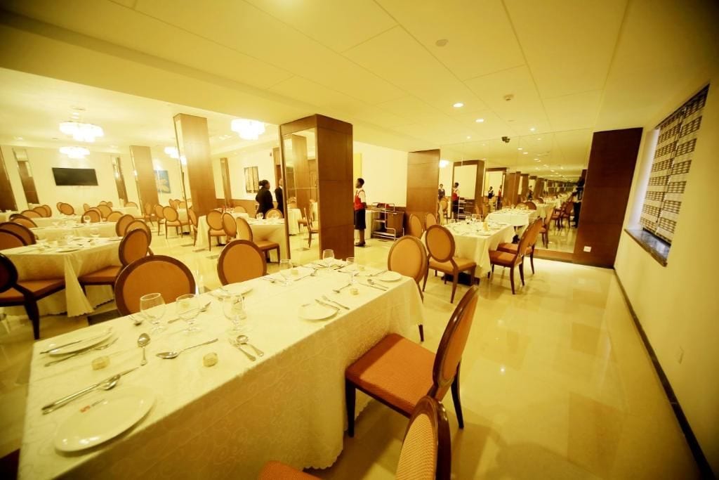 Une salle à manger d’hôtel avec plusieurs tables dressées pour les clients, des chaises et un menu affiché sur un mur.