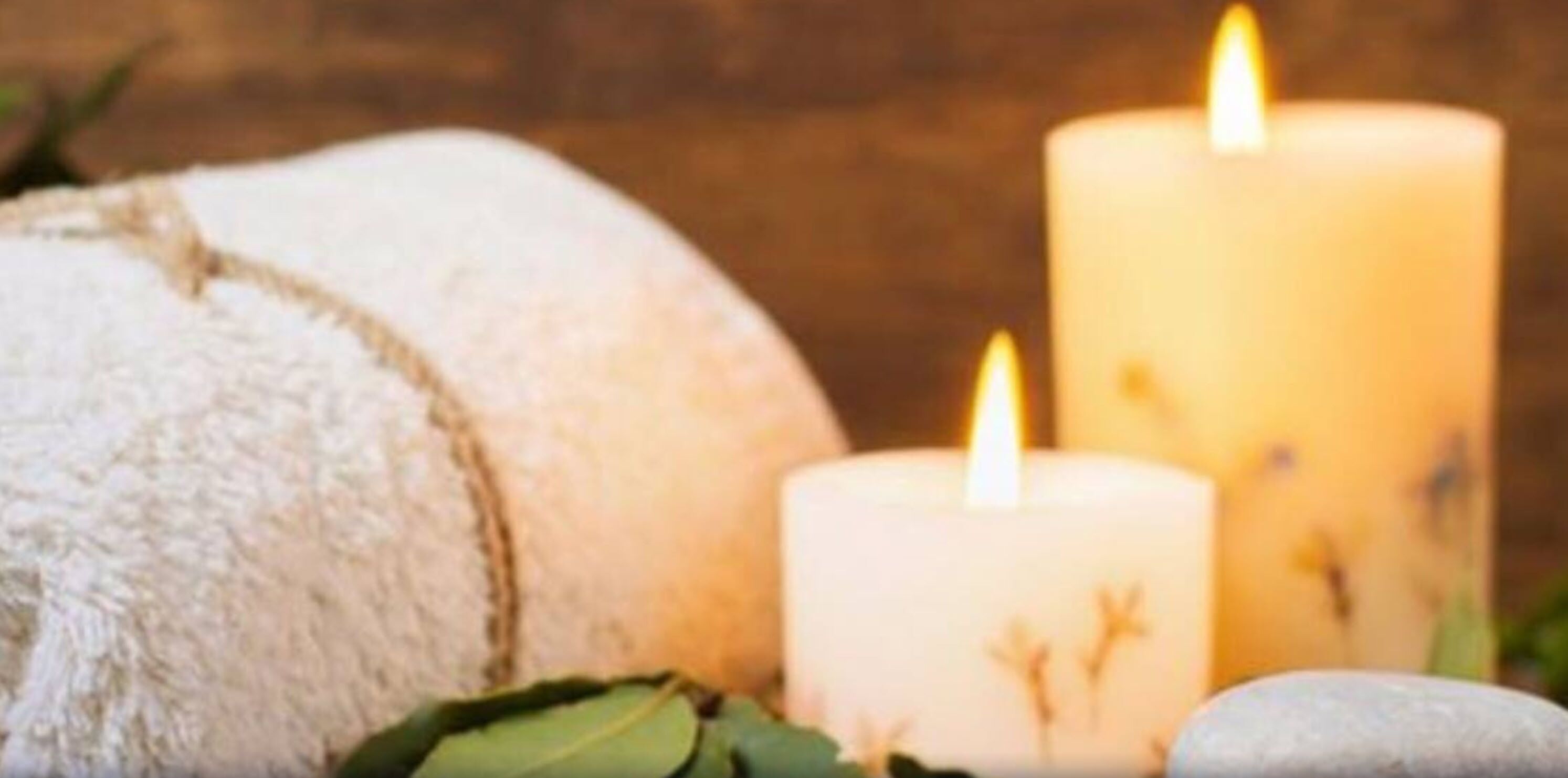 A spa setting with a white towel, two lit candles, and a stone.