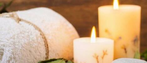 A spa setting with a white towel, two lit candles, and a stone.