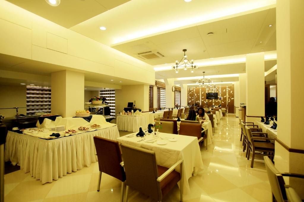 A spacious dining area with multiple tables set for service, a central chandelier, and a clean, modern design.