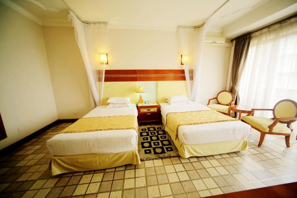 Ein Hotelzimmer mit zwei Betten, einem Nachttisch, einem Sessel und einem Fenster mit Vorhängen.