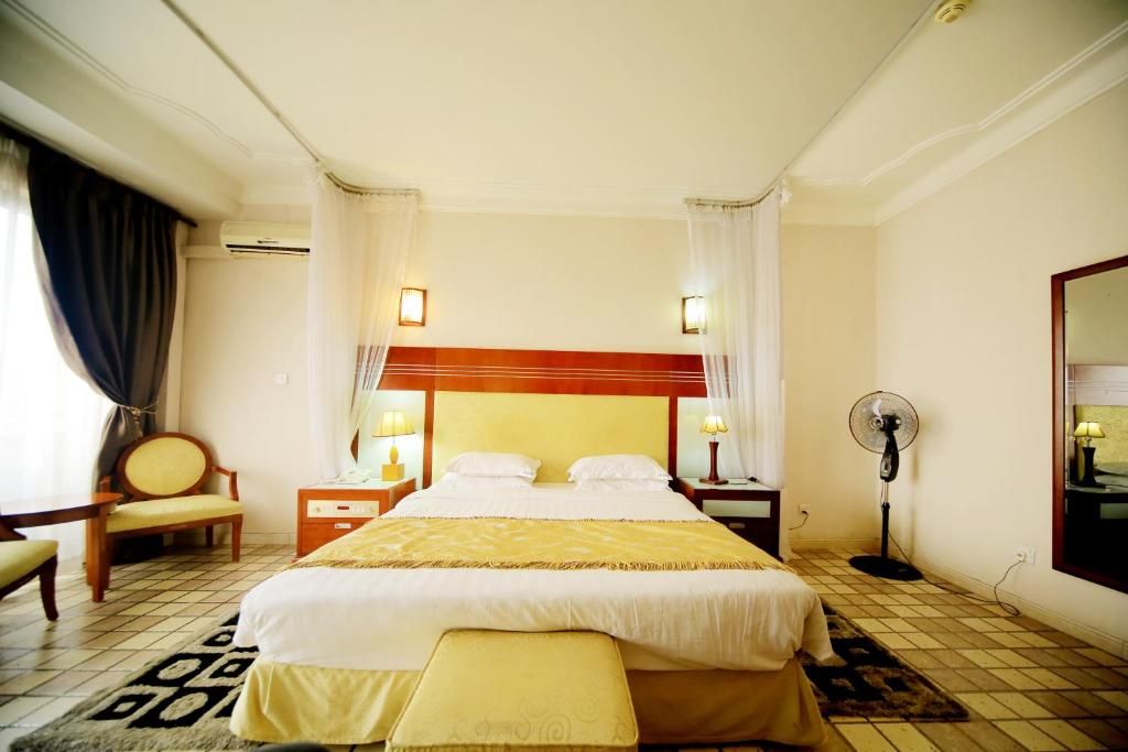 Una habitación de hotel con cama, mesitas de noche, una silla, un ventilador y una ventana con cortinas.