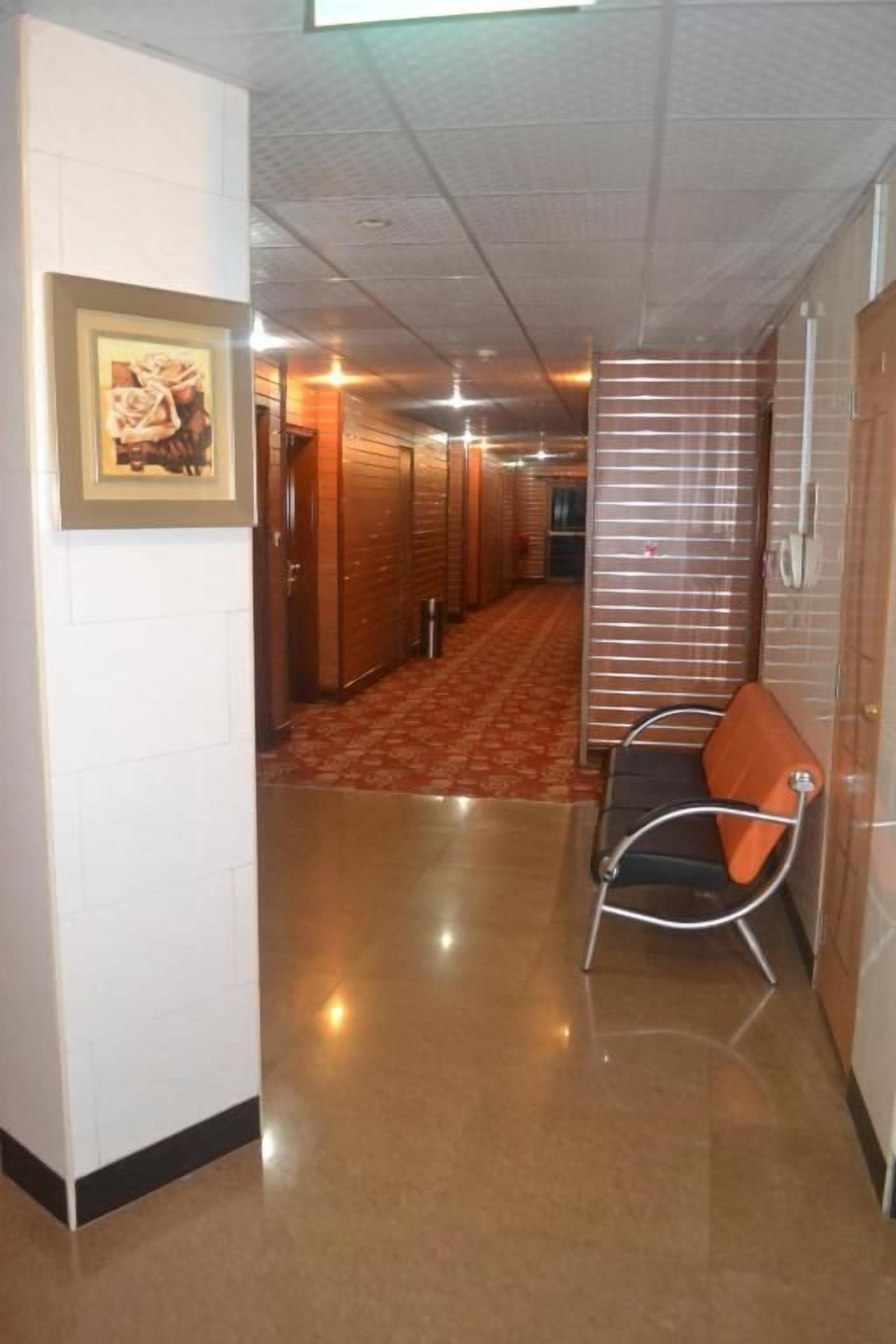 Un couloir d’hôtel avec un sol ciré, un tableau encadré accroché au mur et une rangée de chaises le long du mur.