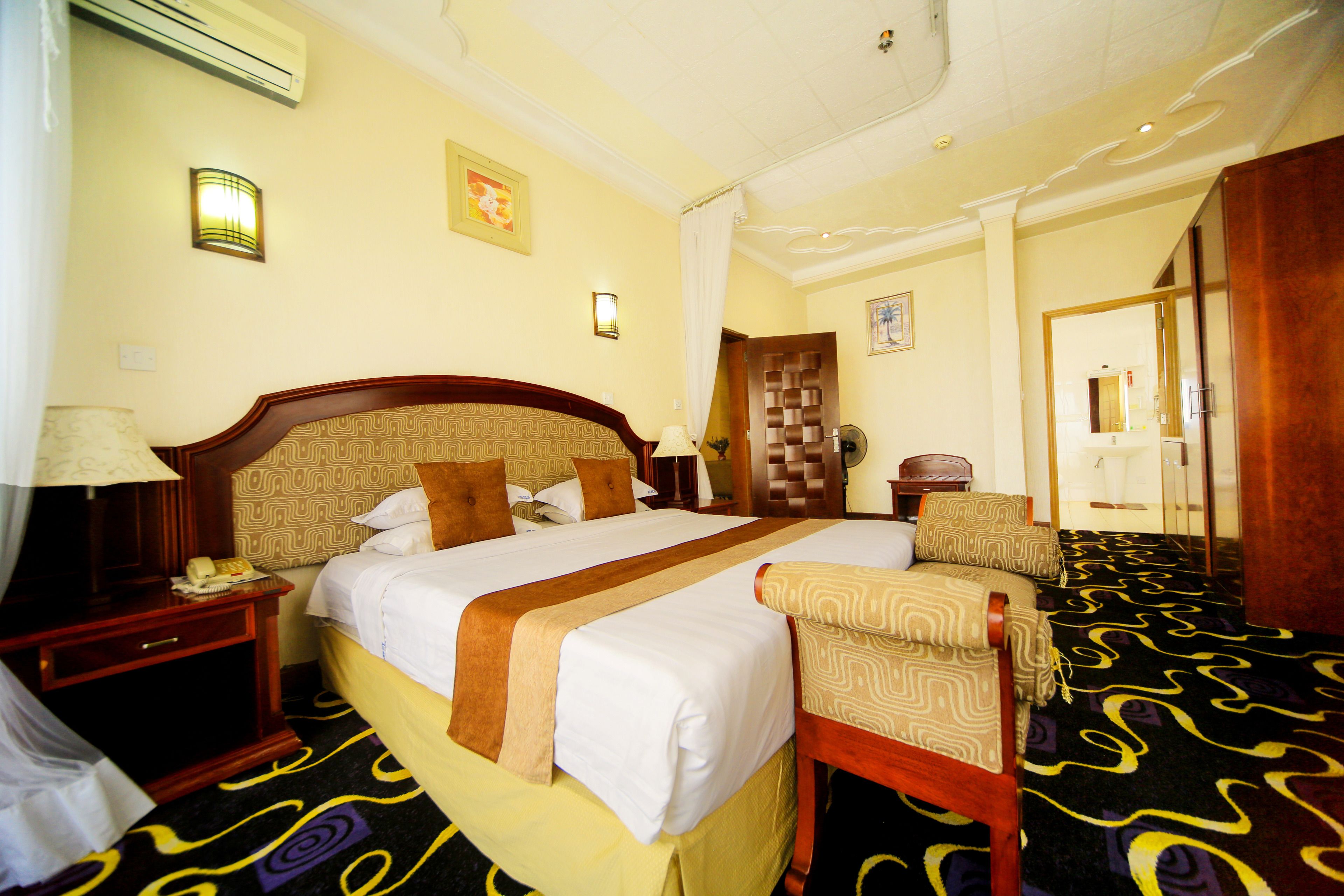 A hotel room with a large bed, a chair, a nightstand, and a lamp.