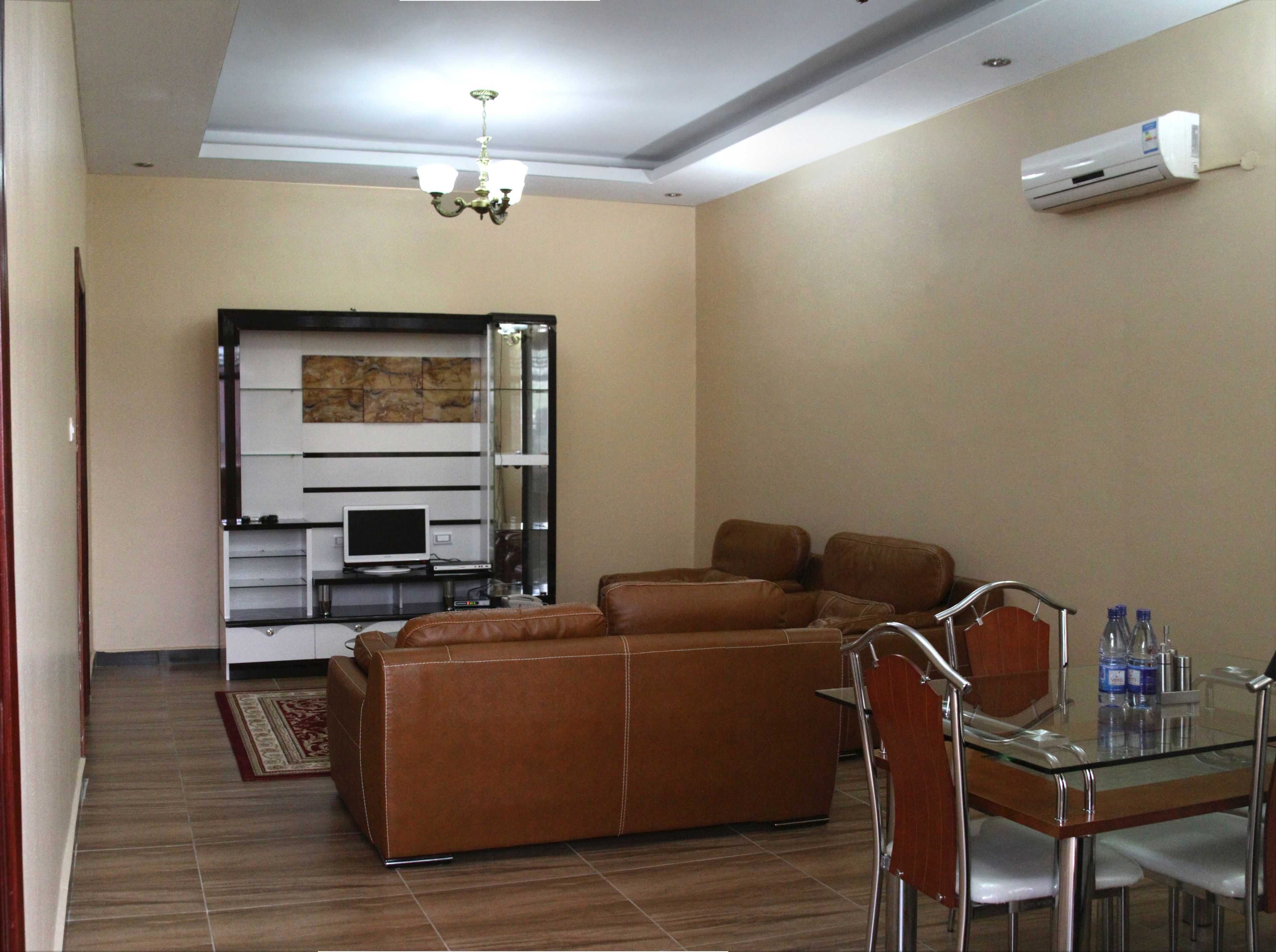 A living room with a brown leather sofa, a glass dining table with chairs, a TV, and a fireplace.