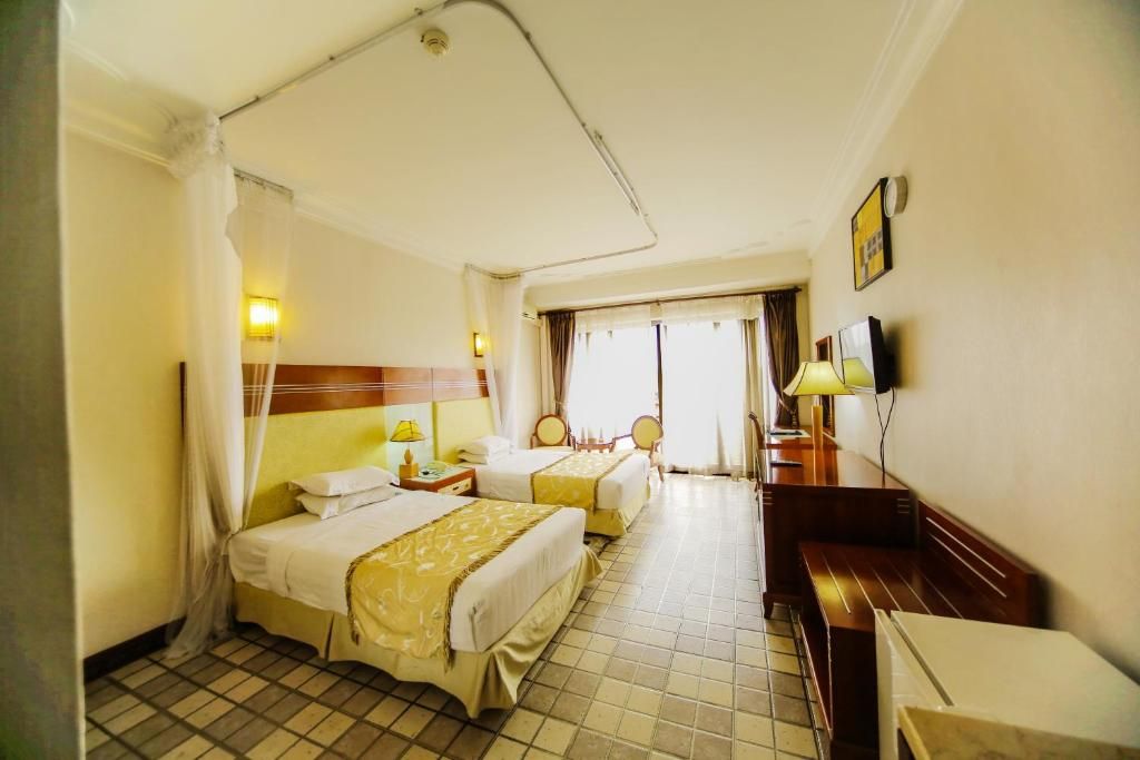 A hotel room with two beds, a desk, a chair, and a television.