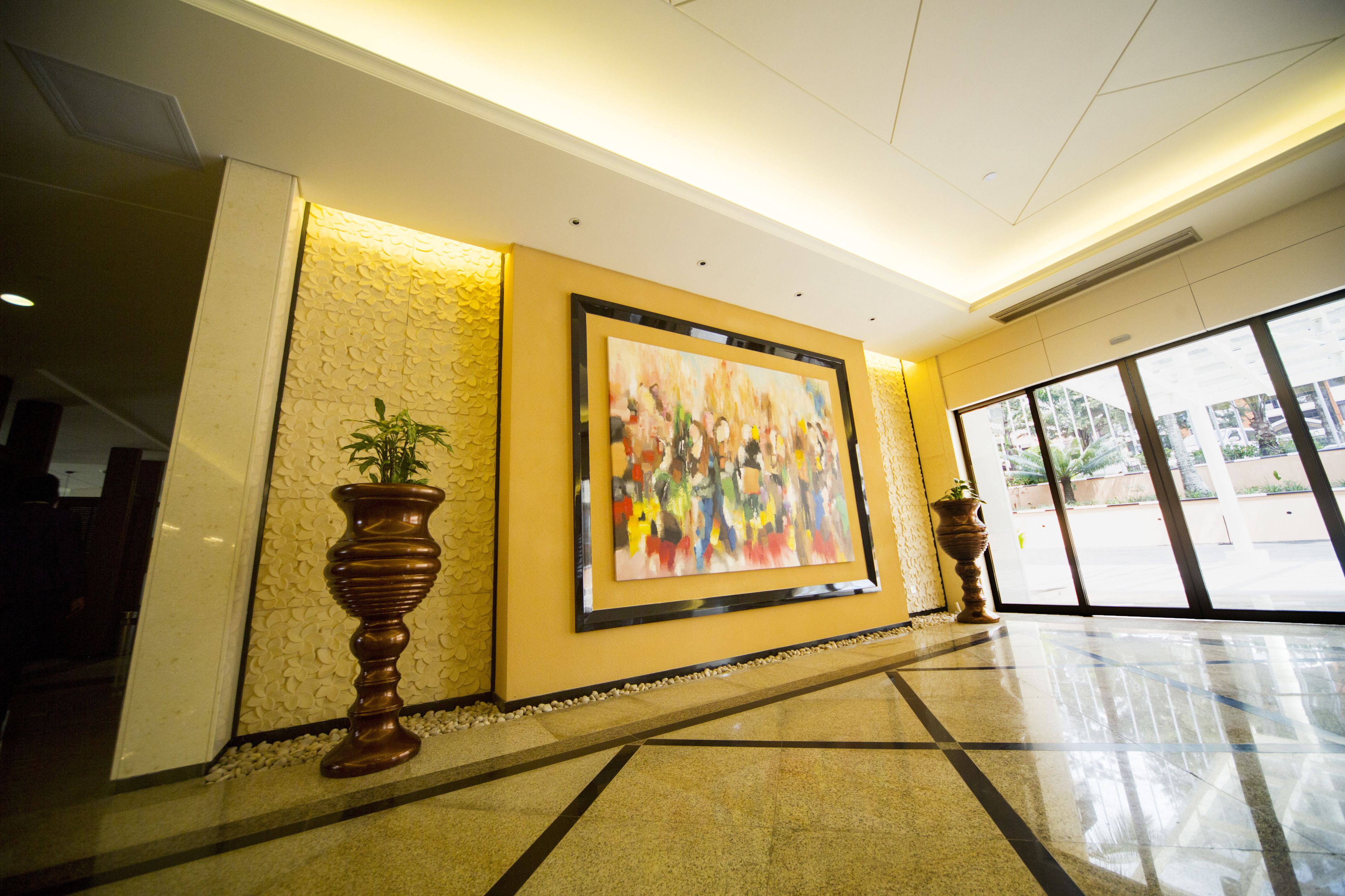 A lobby with a large abstract painting, two potted plants, and a tiled floor.
