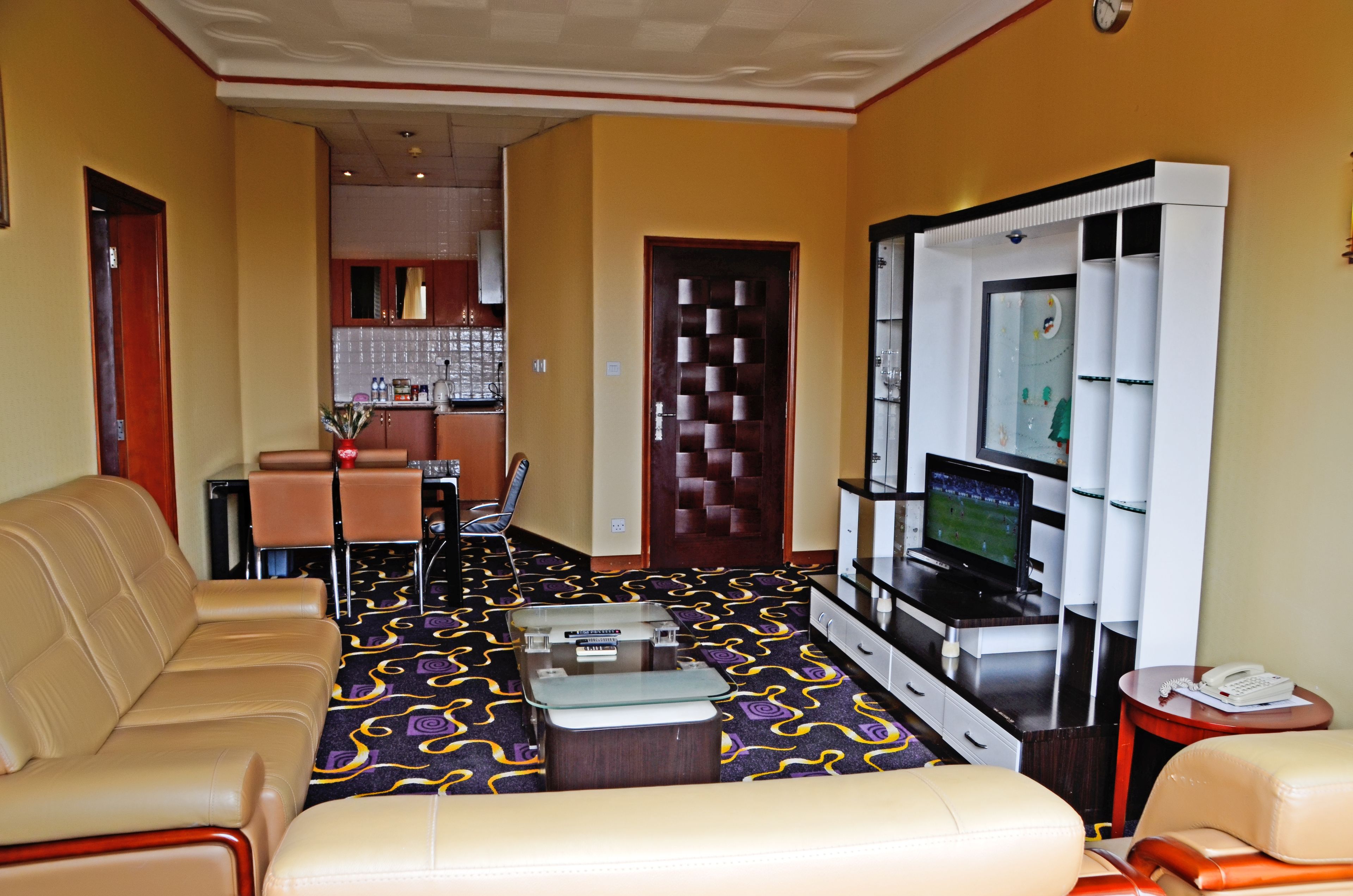A hotel room with a sofa, a TV, a minibar, and a dining area with chairs and a table.