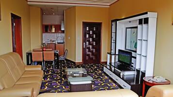 A hotel room with a sofa, a TV, a minibar, and a dining area with chairs and a table.