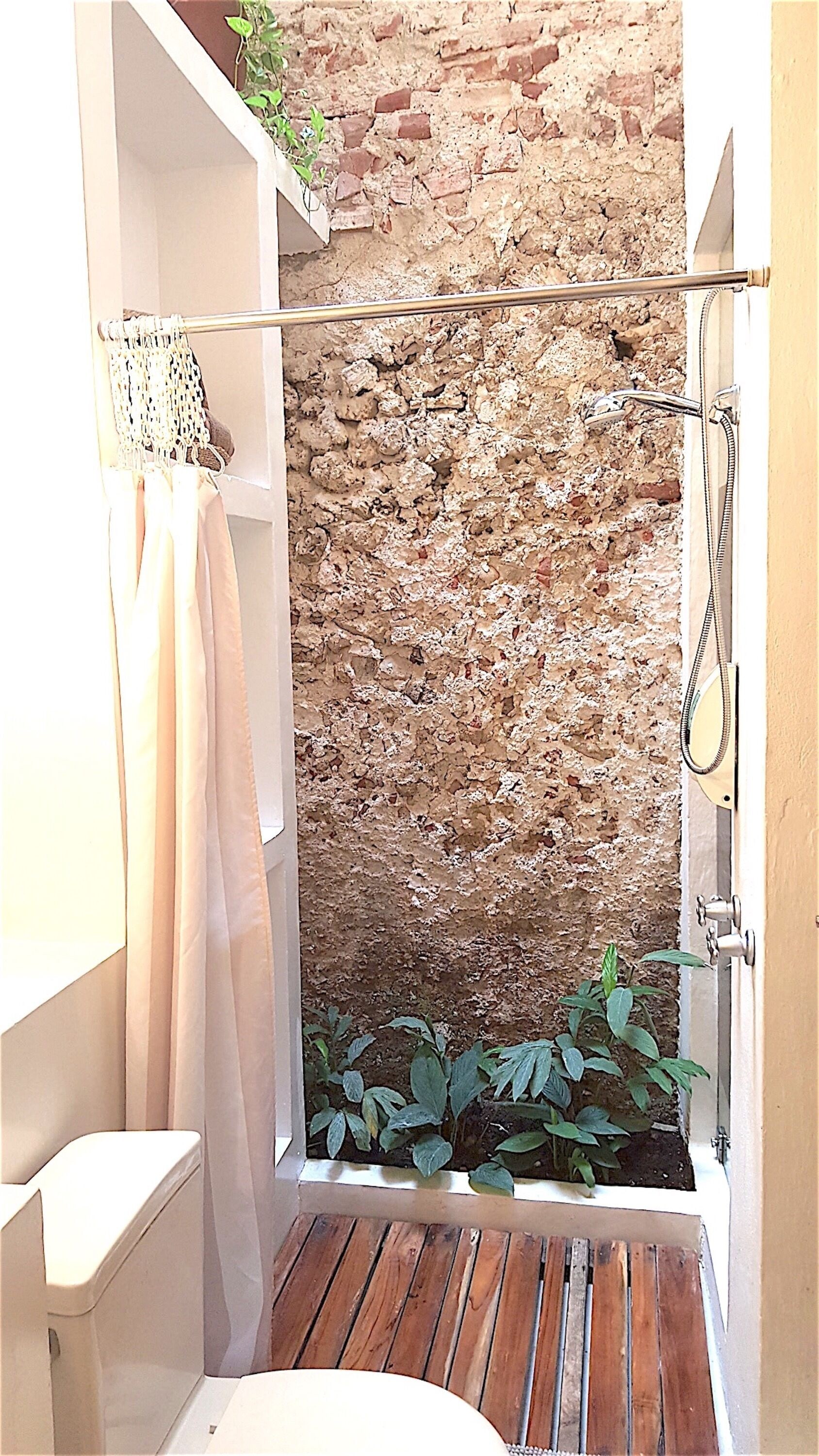 A small, enclosed shower area with a brick wall, wooden floor, and a hanging shower curtain.