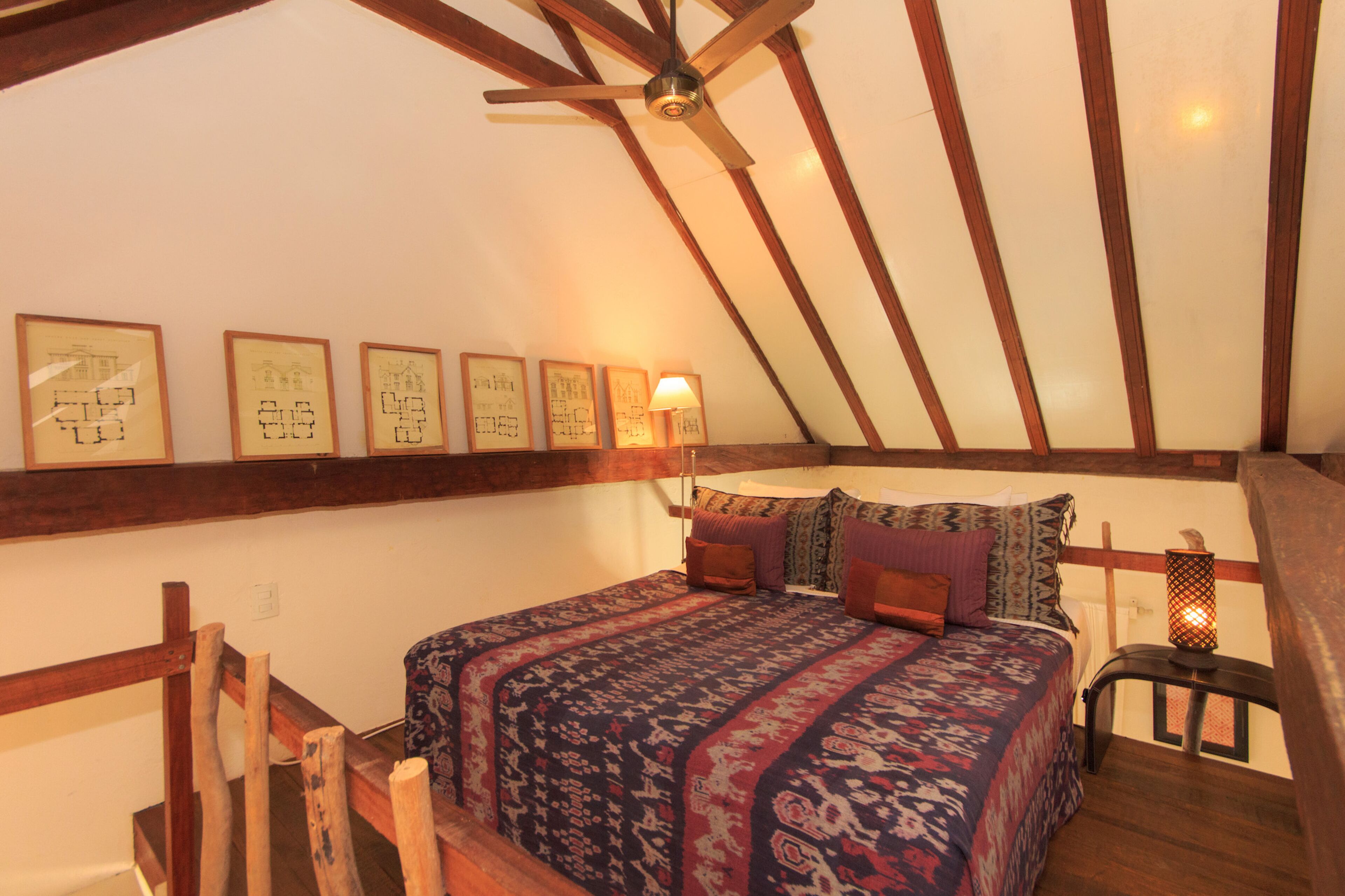 A cozy attic bedroom with a wooden ceiling, a large bed with patterned bedding, and framed artwork on the walls.