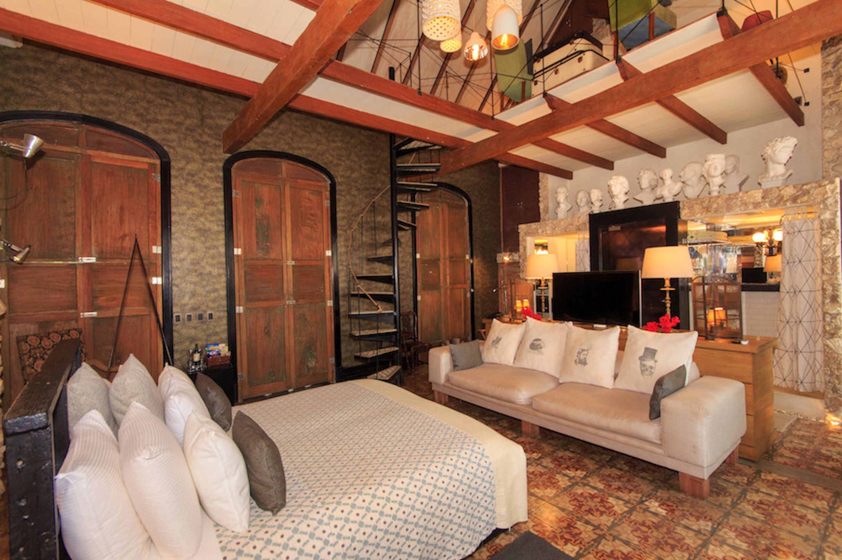 Una habitación acogedora con una cama, un sofá, armarios de madera, un televisor y una escalera.