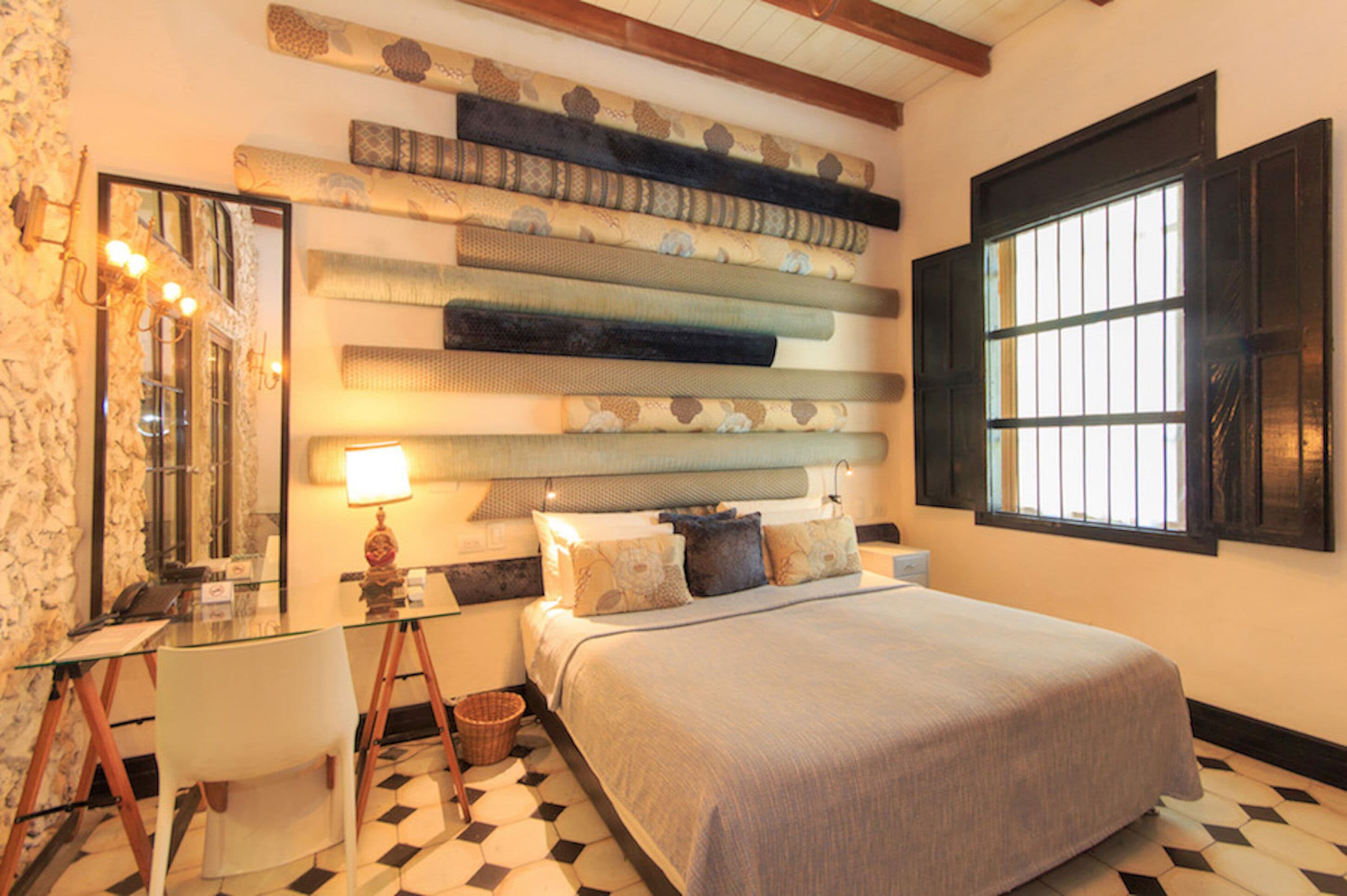 Une chambre à coucher comprenant un lit, une table de chevet, une lampe, une chaise et un mur recouvert d’un tissu à motifs.
