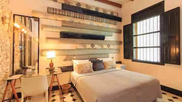 Un dormitorio con cama, mesita de noche, lámpara, silla y una pared con tela estampada.