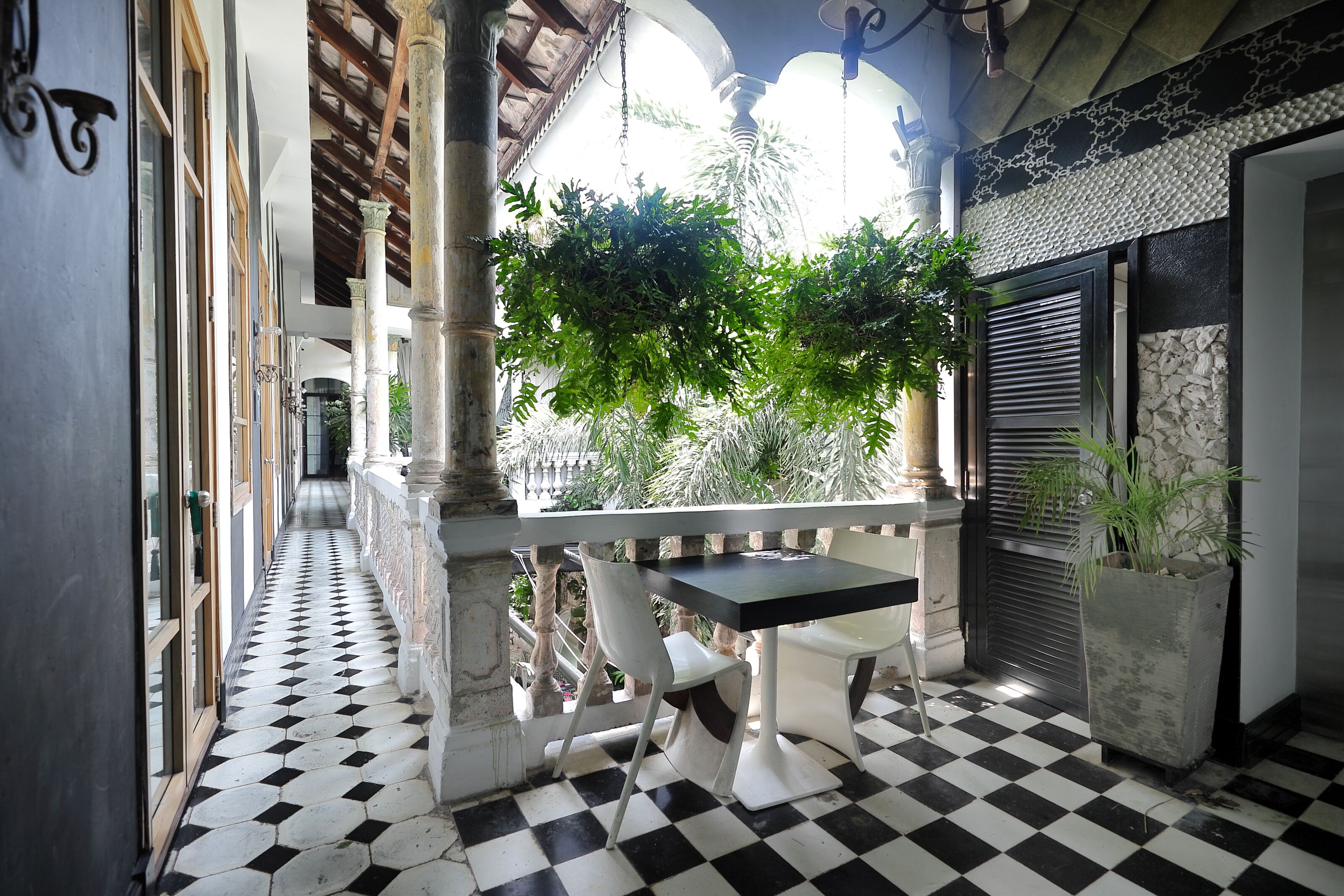 A balcony with a checkered floor, white chairs, a table, and a potted plant.