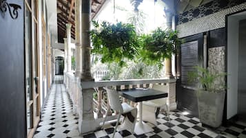 A balcony with a checkered floor, white chairs, a table, and a potted plant.