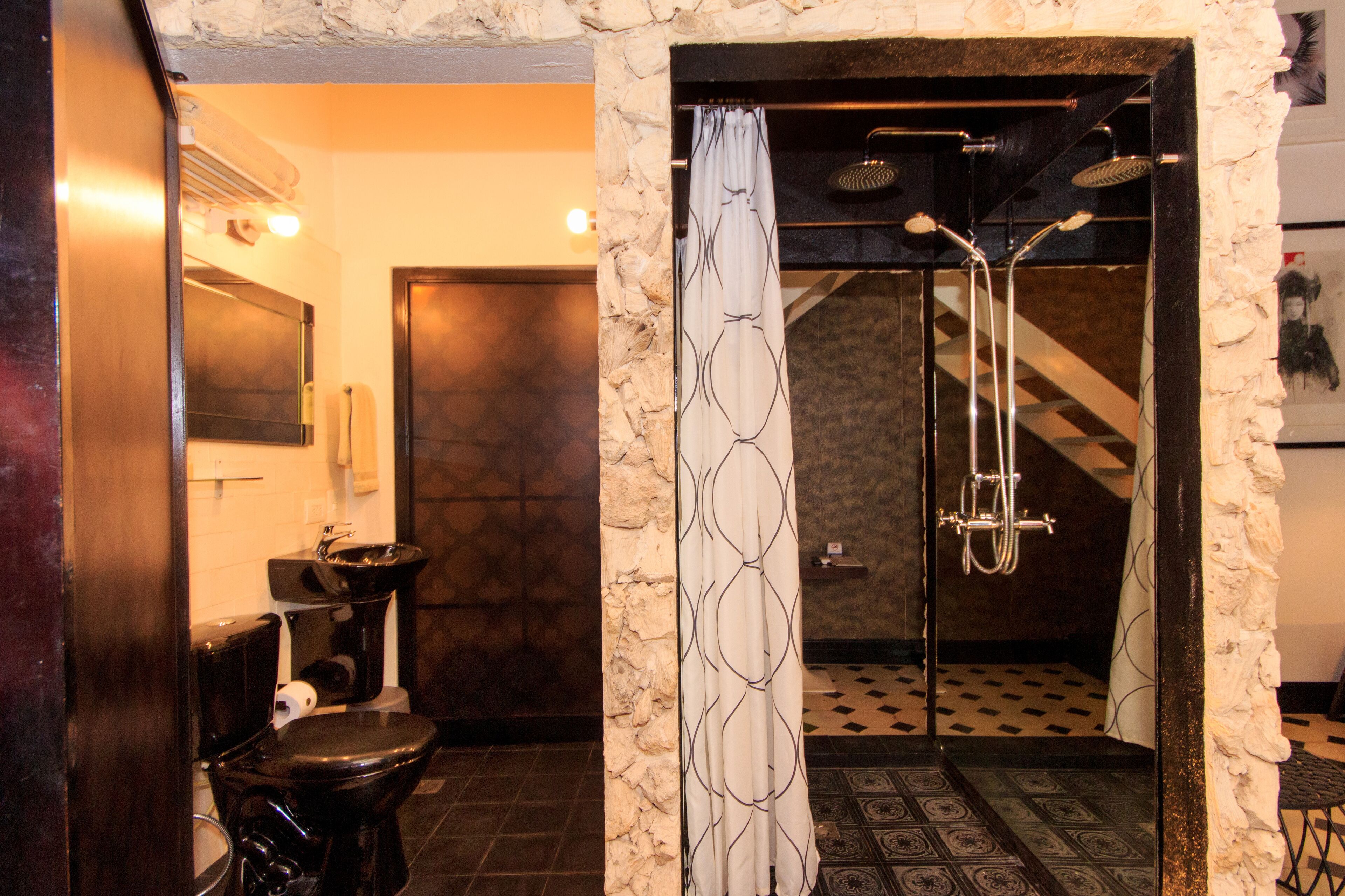 A bathroom with a stone wall, a toilet, a sink, and a shower with a patterned curtain.