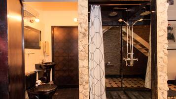 A bathroom with a stone wall, a toilet, a sink, and a shower with a patterned curtain.