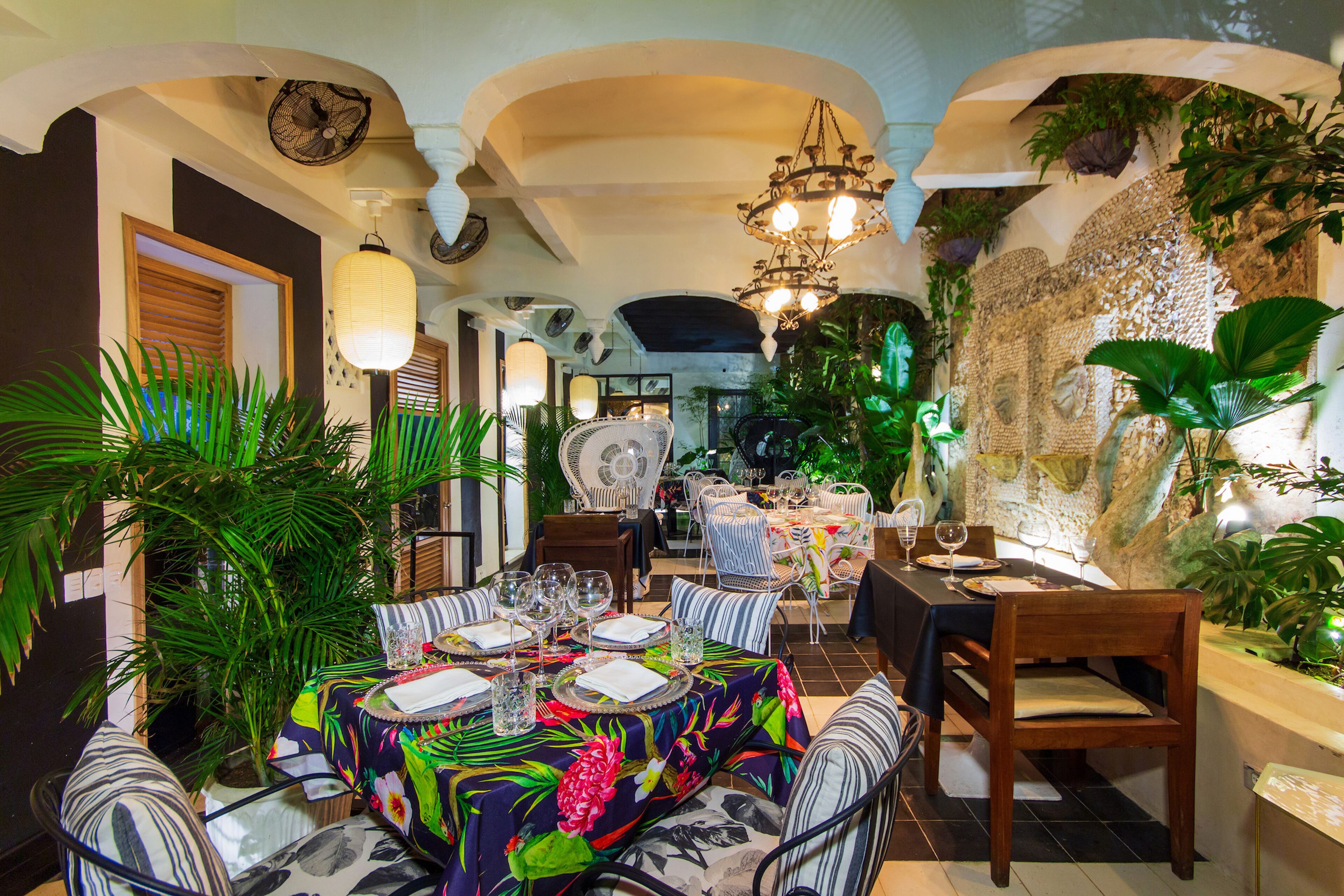 A restaurant with a long table set for dining, surrounded by chairs and plants.
