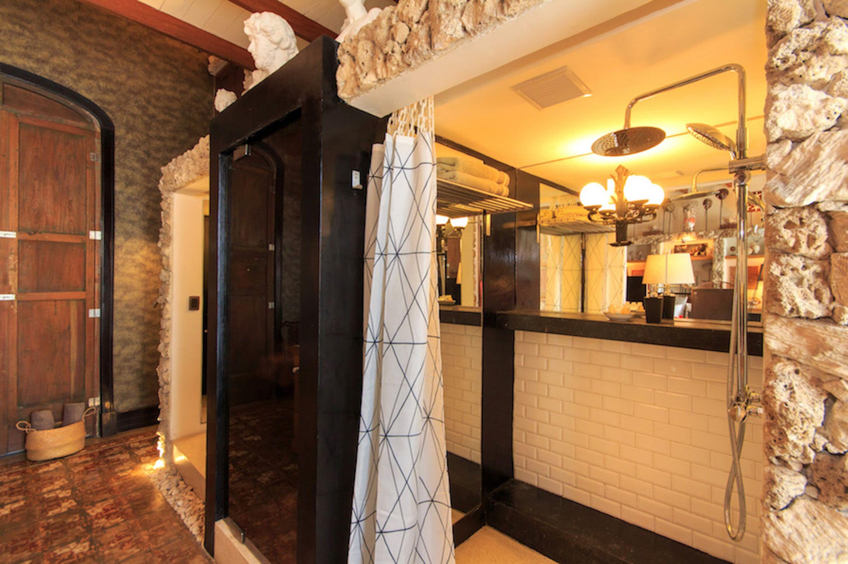 A bathroom with a stone wall, a wooden door, a shower with a glass enclosure, and a mirror with a towel rack.