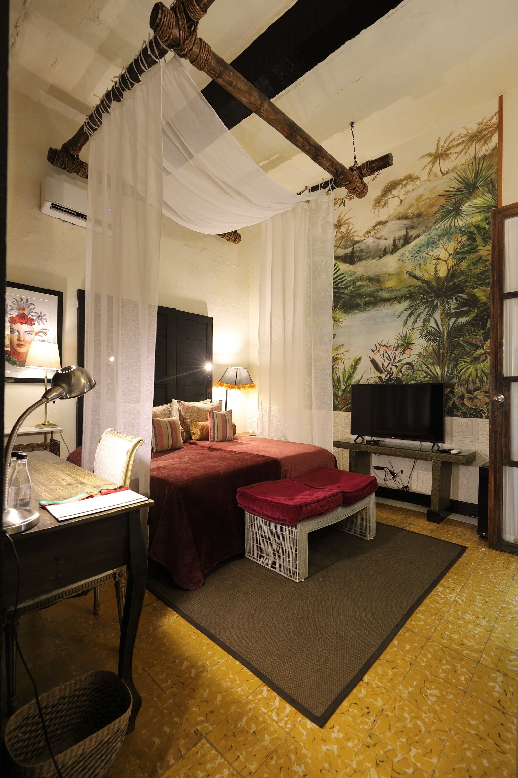 A room with a bed, a desk, a television, and a mural on the wall.