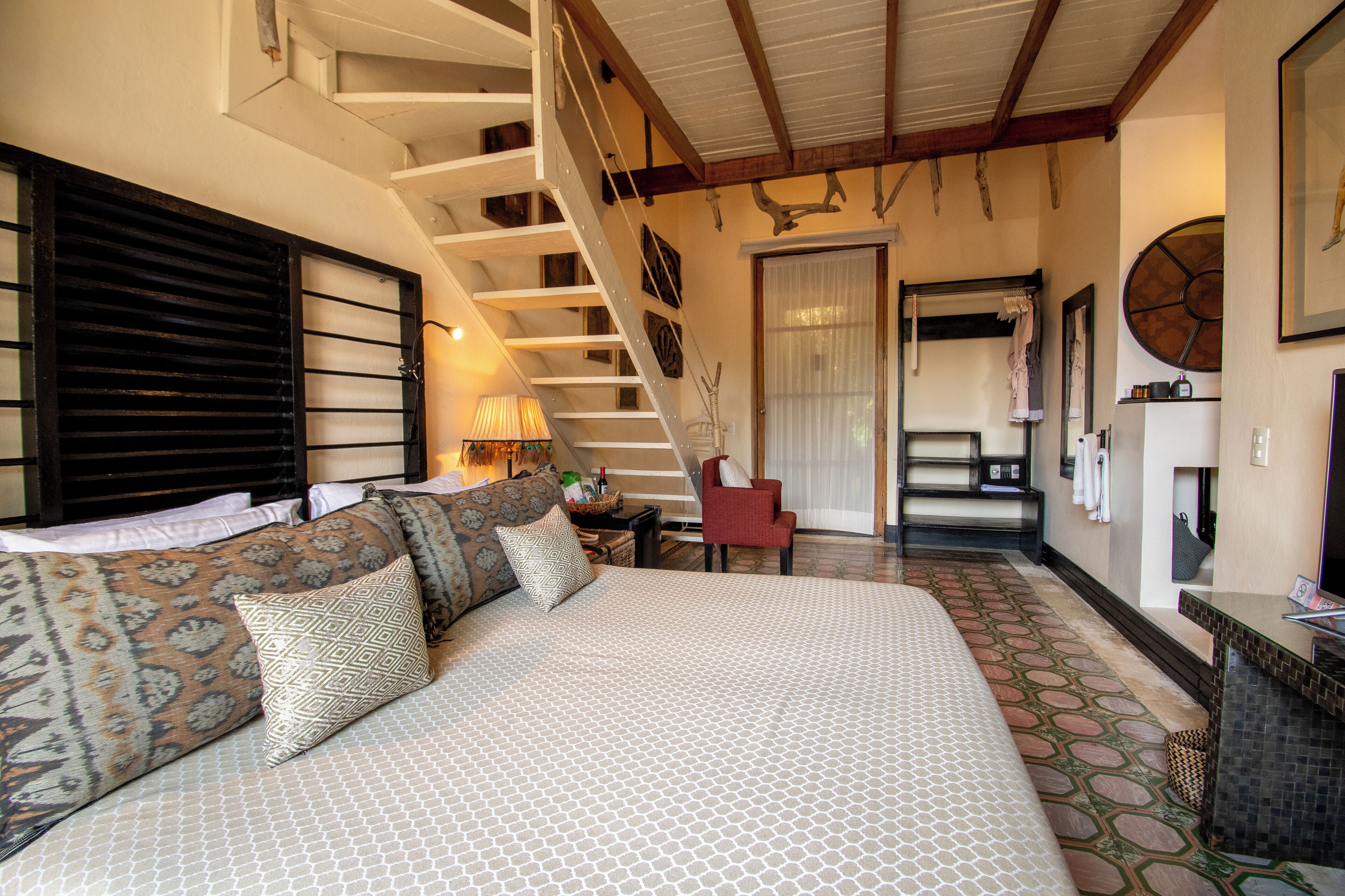 A spacious bedroom with a large bed, a staircase, and a bathroom with a large mirror and a clock.