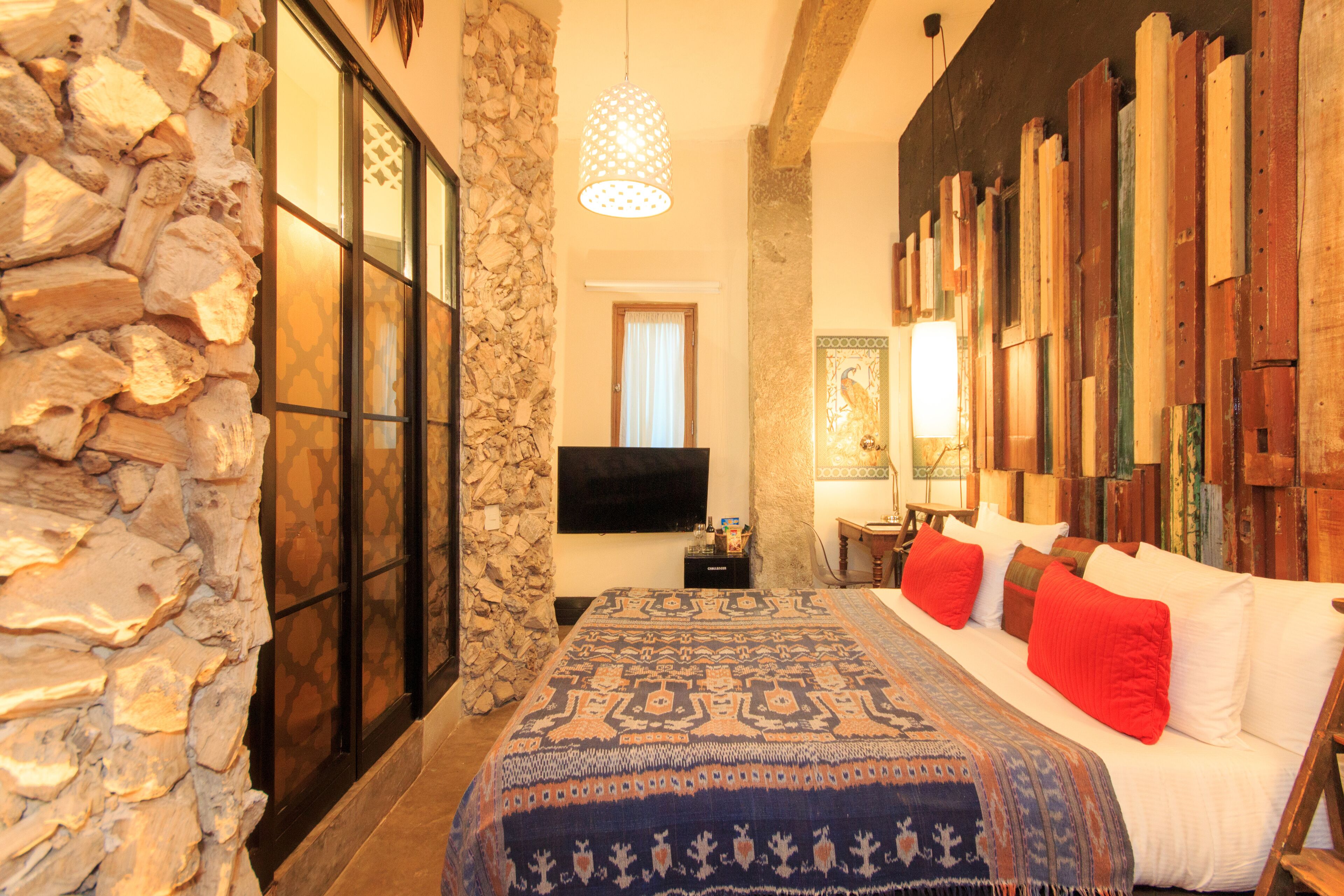 A bedroom with a stone wall, a bed with a patterned bedspread, and a wooden headboard.