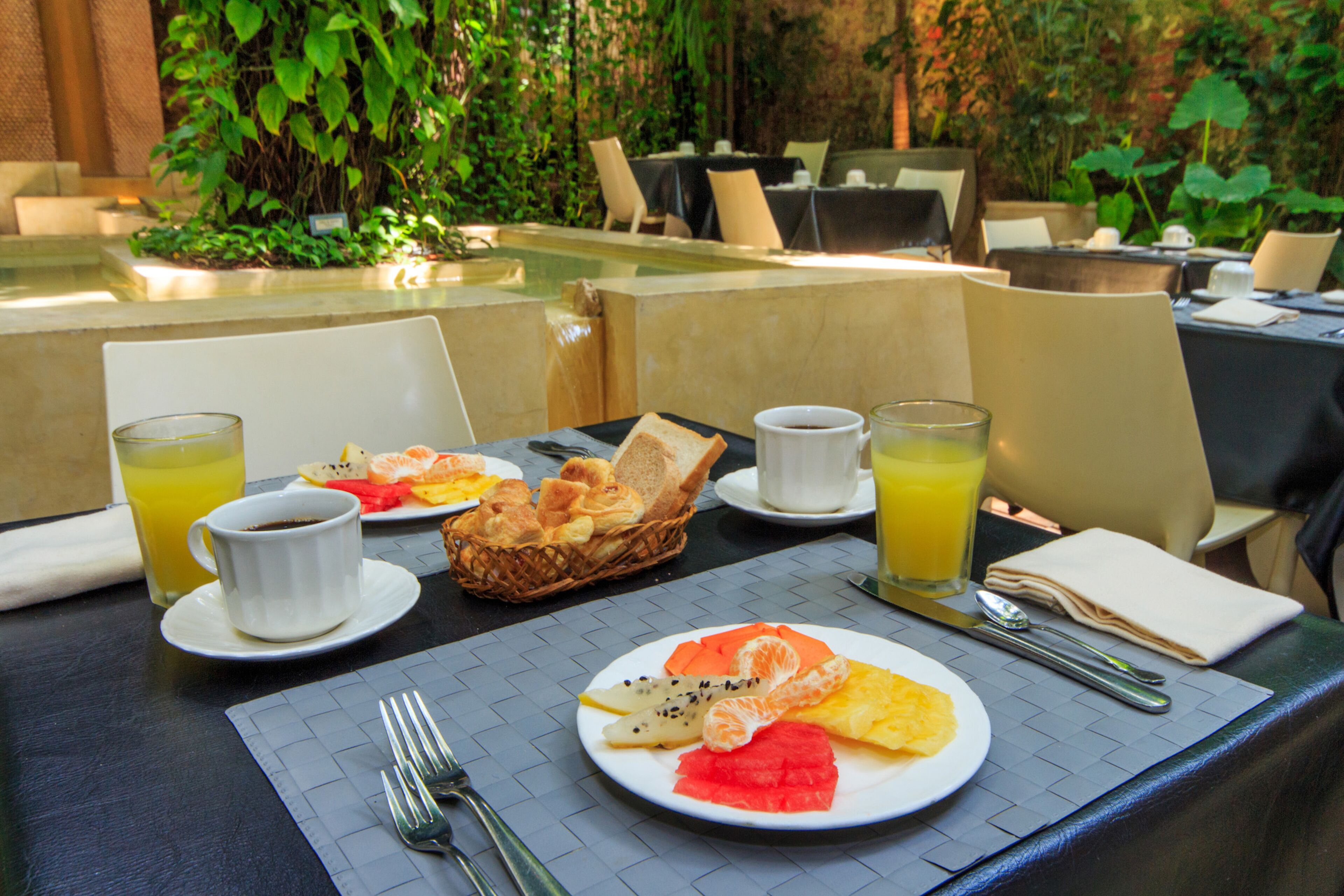 Une table mise pour le petit-déjeuner, avec des assiettes de fruits, des croissants et du jus d’orange.