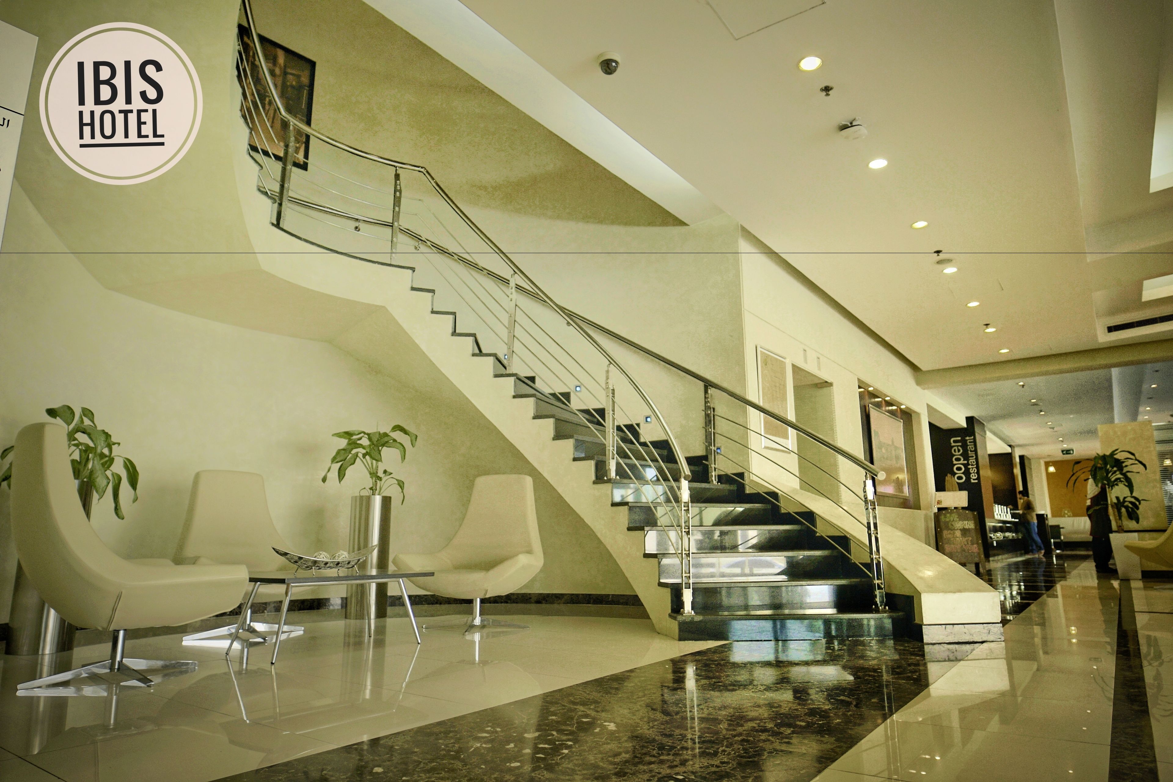 A modern hotel lobby with a marble floor, a staircase, and seating areas.