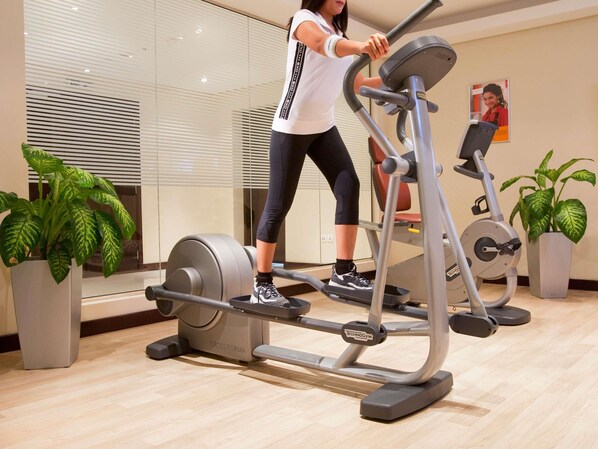 Una persona usando una máquina elíptica en un gimnasio con plantas en macetas y un cartel en la pared.