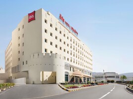 A hotel with a prominent 'ibis Hotel' sign, a large entrance with a covered area, and a landscaped garden in front.