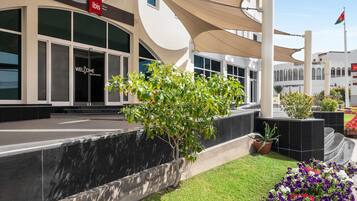 Entrada de hotel con un letrero que dice 'Welcome to My World', un área exterior techada con un árbol y un cantero de flores.