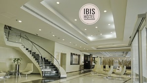 Un hall d'hôtel moderne doté d'un escalier central, de coins salon et d'une enseigne bien visible indiquant « HÔTEL IBIS ».