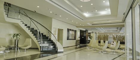 A modern hotel lobby with a central staircase, seating areas, and a prominent 'IBIS HOTEL' sign.