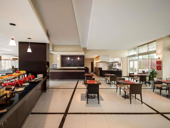 A modern hotel lobby with a reception desk, dining area, and kitchen in the background.