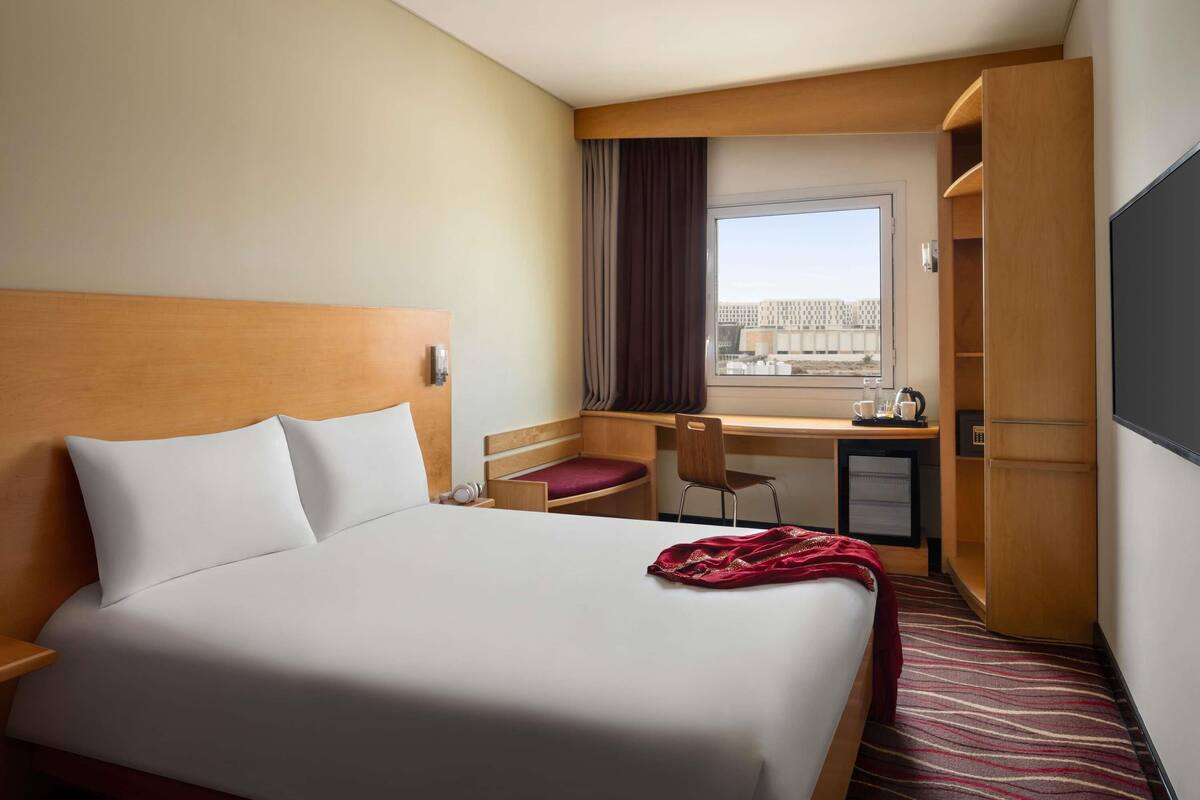 Habitación de hotel con cama, escritorio, silla y vista a un edificio por la ventana.