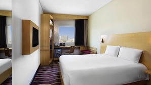 Une chambre d’hôtel équipée d’un lit, d’un bureau, d’une chaise, d’une télévision et offrant une vue sur la ville.