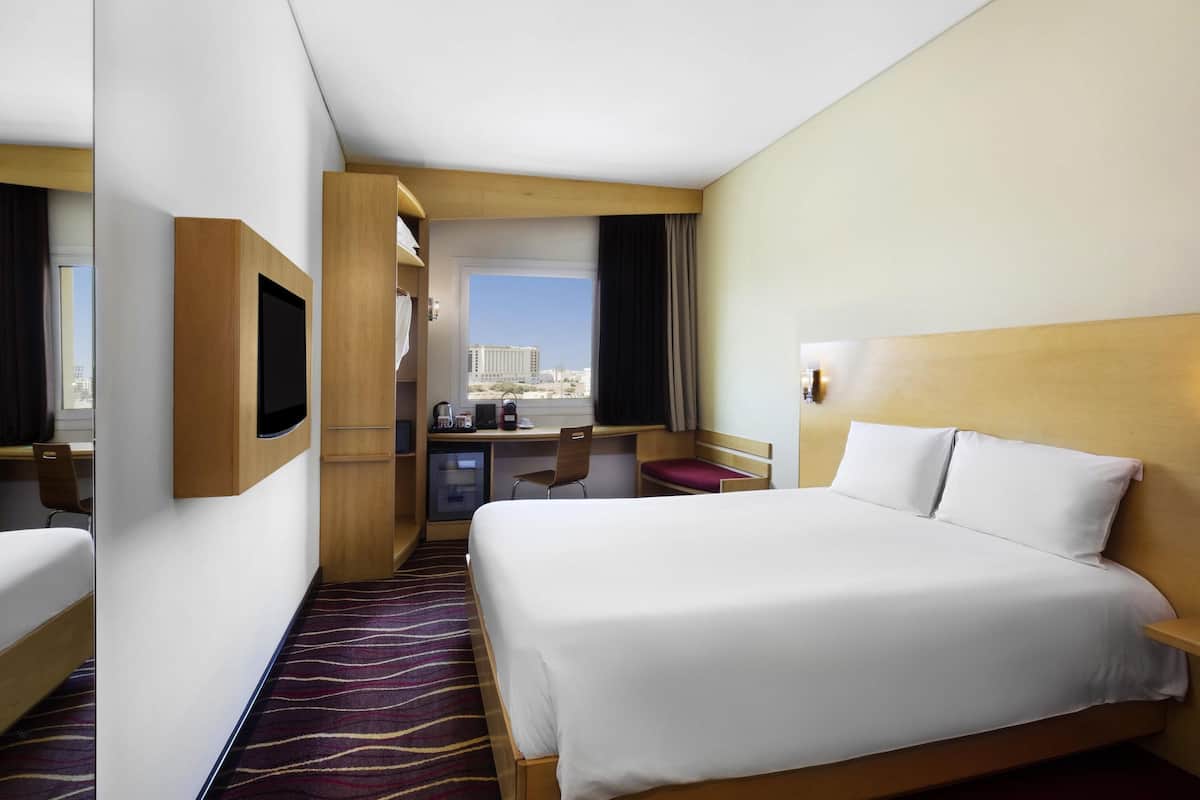 Habitación de hotel con cama, escritorio, silla, televisión y vistas a la ciudad.