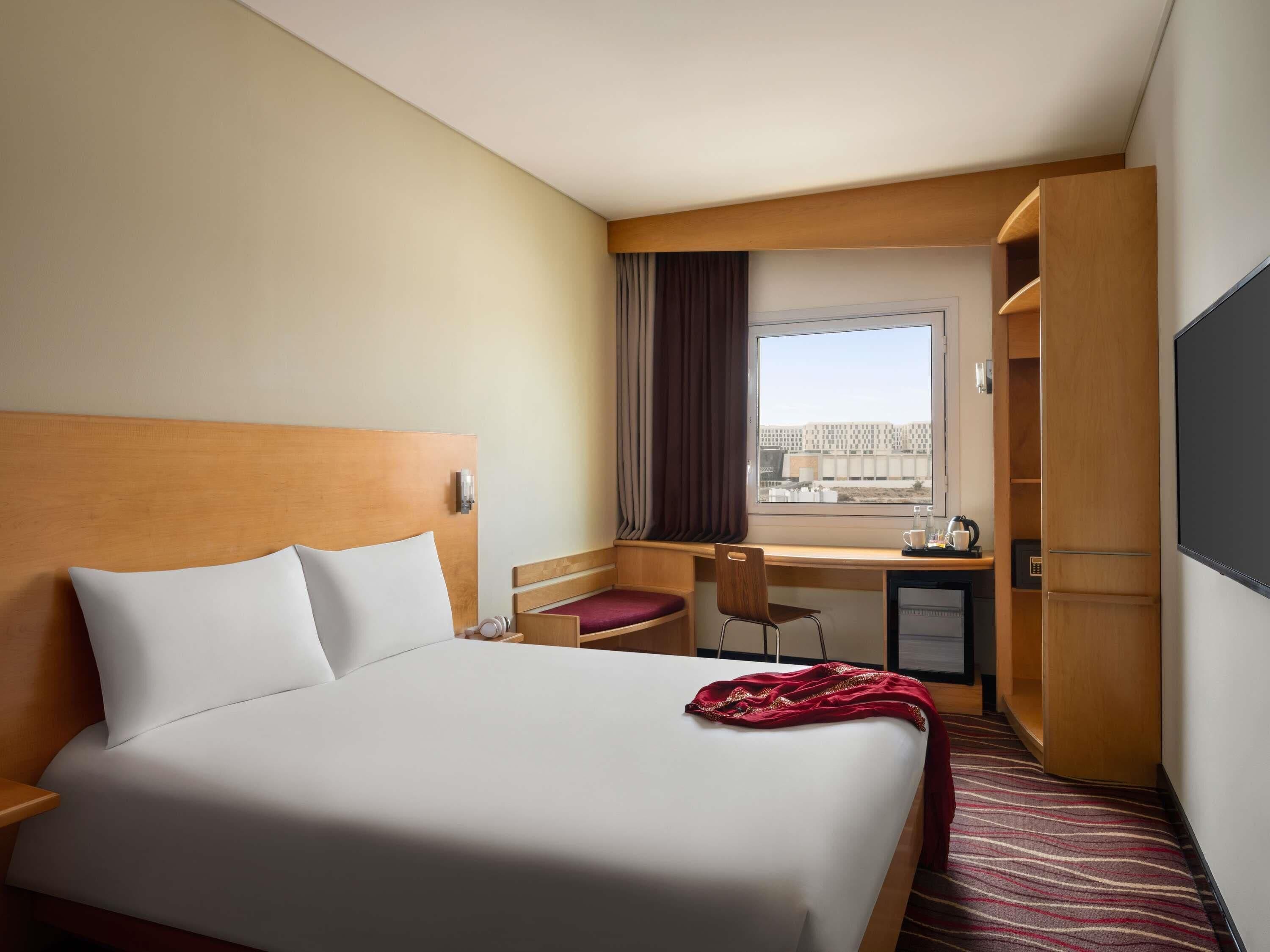 A hotel room with a bed, desk, chair, and a view through the window.